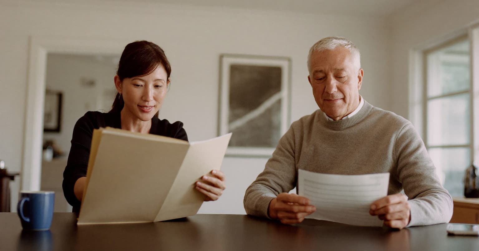 Small-business owner sorting tax forms while her accountant reviews a page at a kitchen table